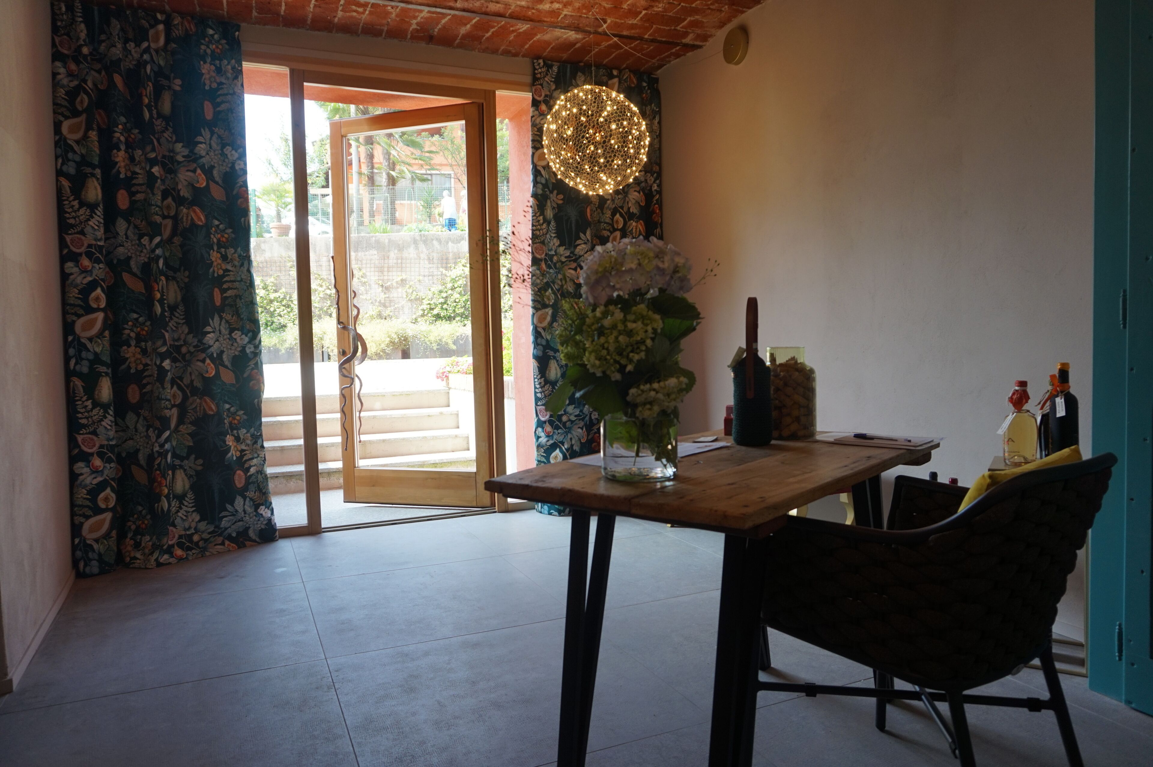 A room with a wooden table, a vase with flowers, a hanging light fixture, and a view through a glass door.