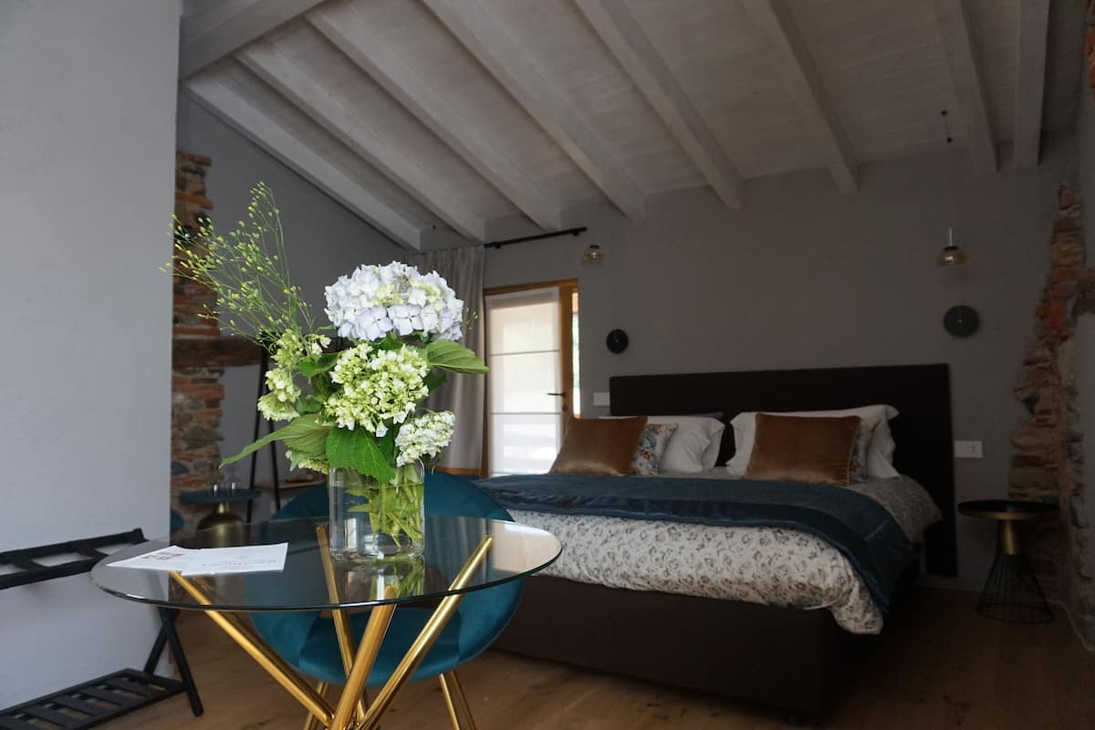 A bedroom with a bed, a glass table with a vase of flowers, and a view of the outside.
