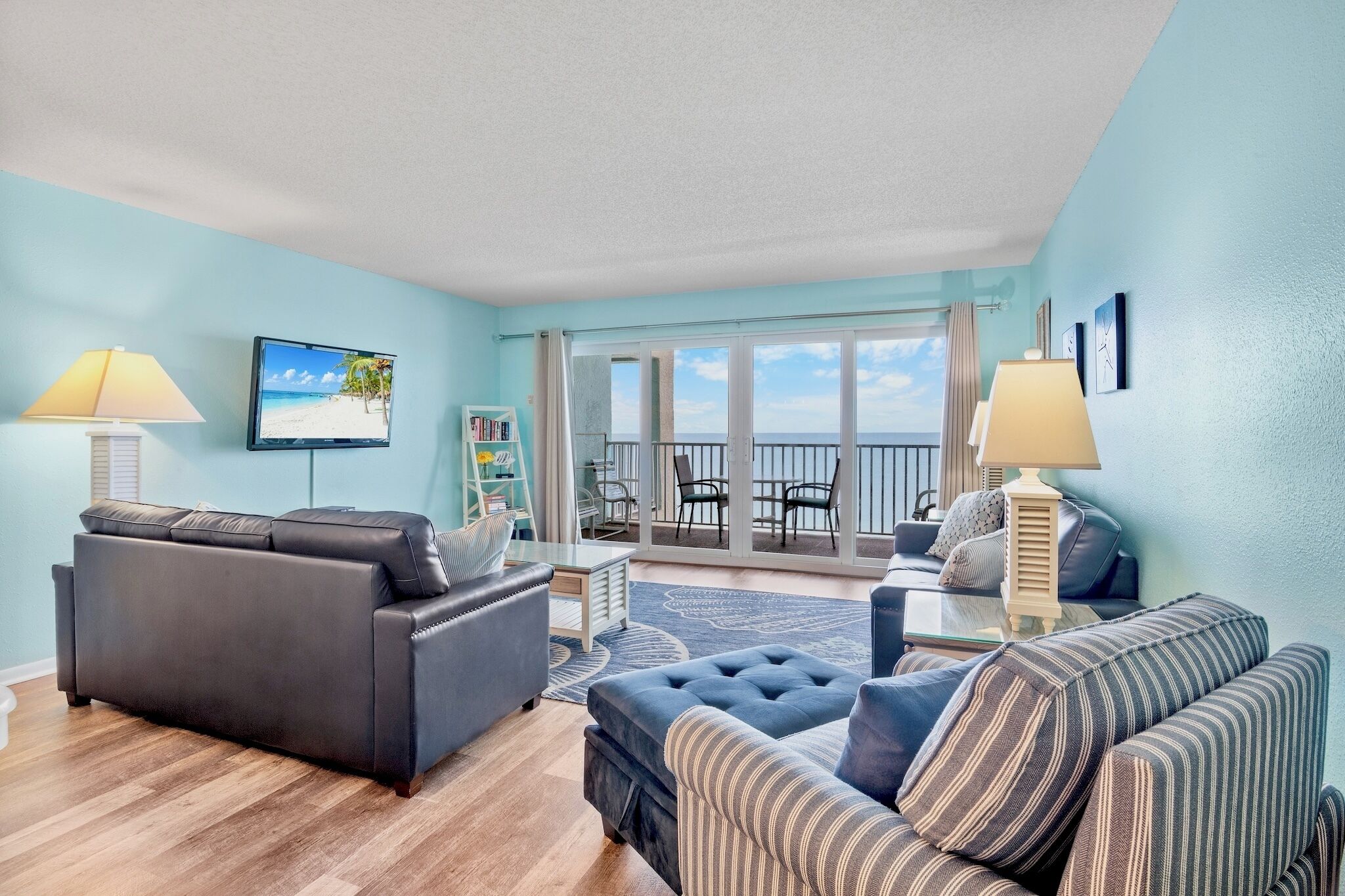 A living room with a sofa, armchair, and a television displaying a beach scene.