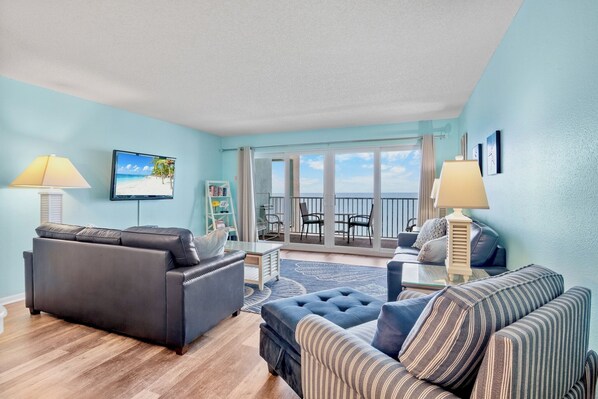 A living room with a sofa, armchair, and a television displaying a beach scene.