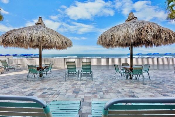 A beachside patio with thatched umbrellas, green chairs, and a view of the ocean.