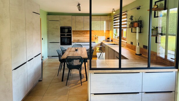 Una cocina moderna con comedor, que incluye una mesa y sillas de madera, horno empotrado y un amplio ventanal con plantas.