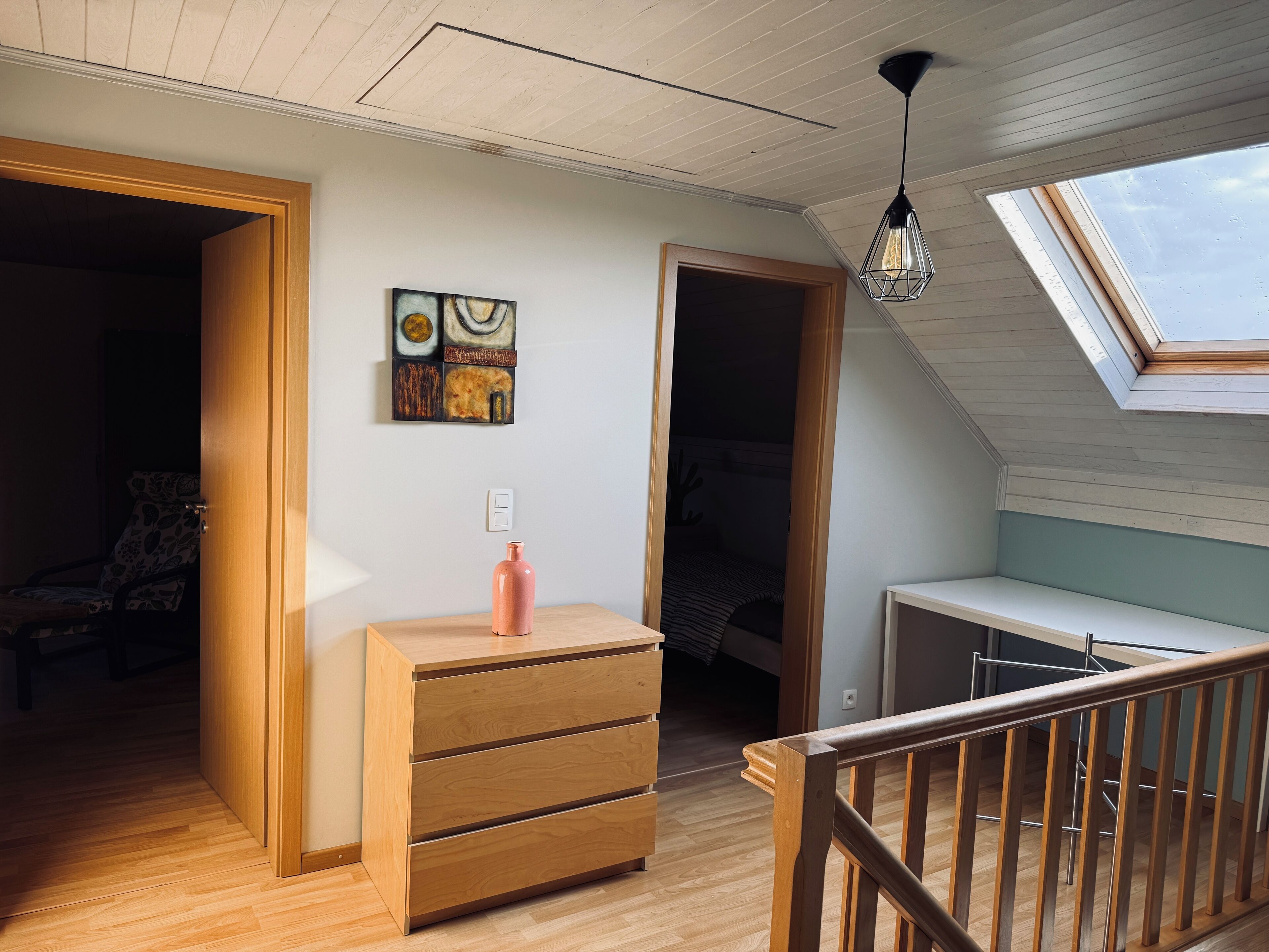Een kamer met een houten dressoir, een schilderij aan de muur en een dakraam.