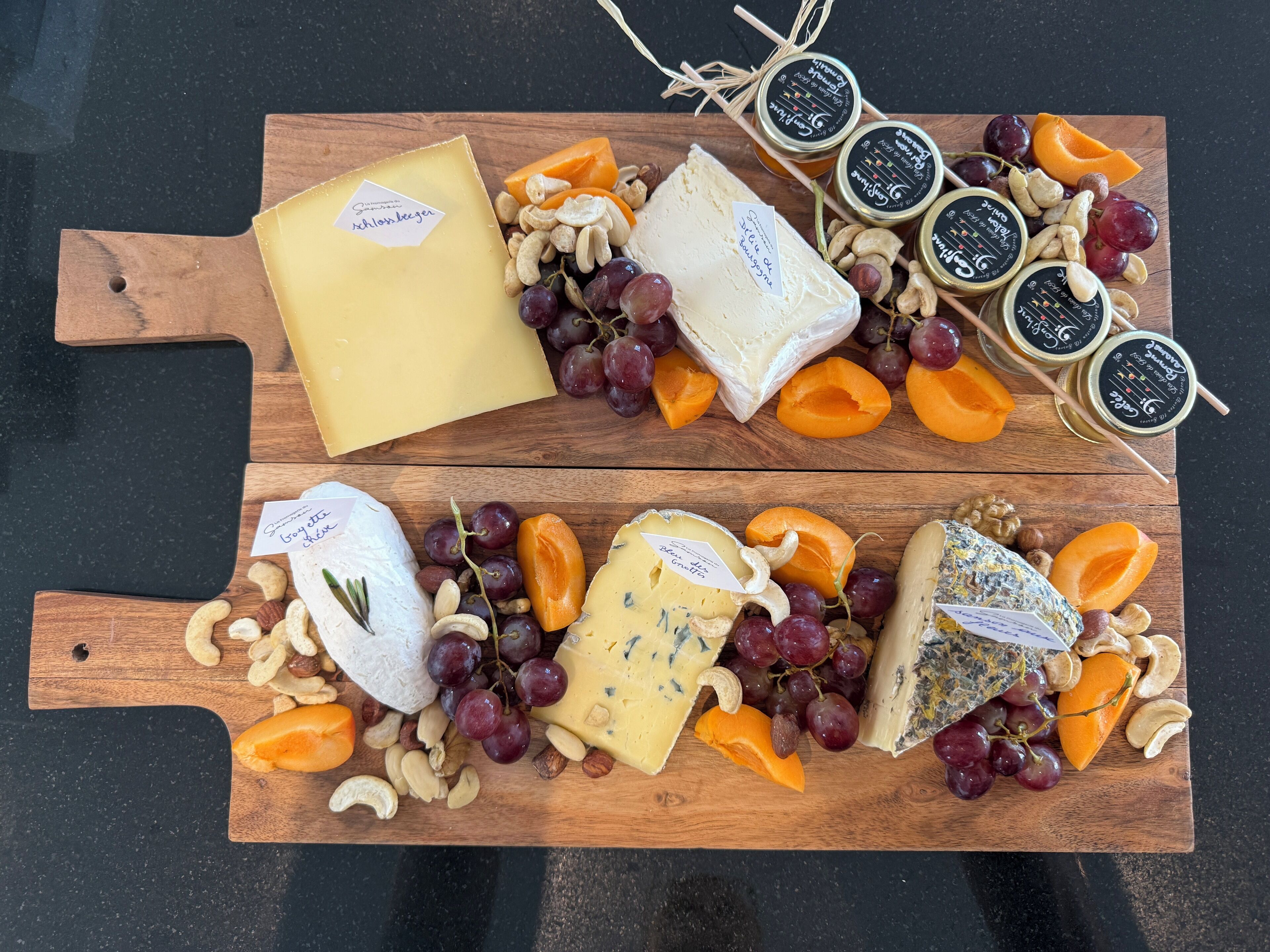 Une planche en bois garnie de différents fromages, de raisins et d’abricots.
