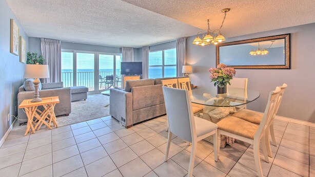 A modern living room with a glass dining table, white chairs, a sofa, and a TV.