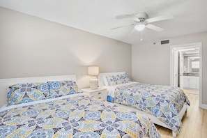 A bedroom with two beds, a ceiling fan, and a nightstand with a lamp.