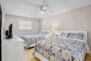 A bedroom with two beds, a ceiling fan, a TV, and a window with blinds.