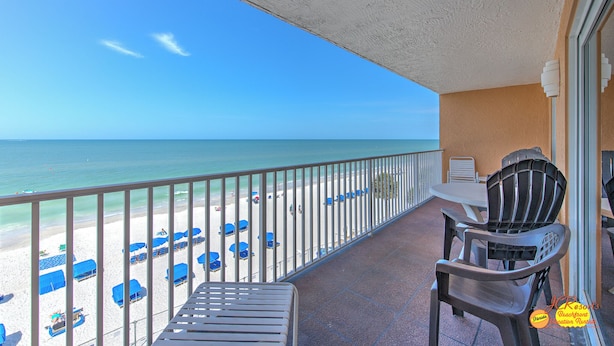 A balcony with a view of the beach, a table, and two chairs.