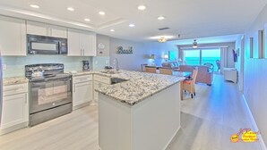A modern kitchen with stainless steel appliances, a large island, and a view to the living area.
