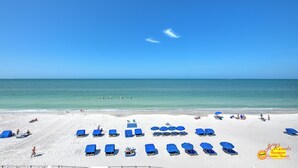 A beach with rows of blue beach chairs and umbrellas, a sandy shore, and the ocean in the background.