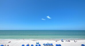 Una playa con filas de sillas azules y sombrillas, una orilla arenosa y el océano al fondo.