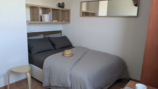 A neatly arranged bedroom with a bed, a small wooden nightstand, a mirror, and a bedside table with a cup. - Studio at the gates of the Avignon ramparts (Avignon)