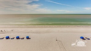 A beach with rows of blue beach chairs and a clear view of the ocean.