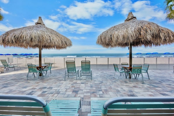 Eine Terrasse am Strand mit StrohdĂ€chern, grĂŒnen StĂŒhlen und Blick aufs Meer.