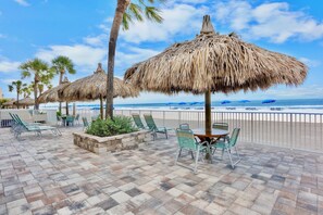 A beachside patio with thatched umbrellas, lounge chairs, and a table with chairs. - Top Floor Gulf Front Huge Condo w/ Balcony RS506 (N. Redington Beach)