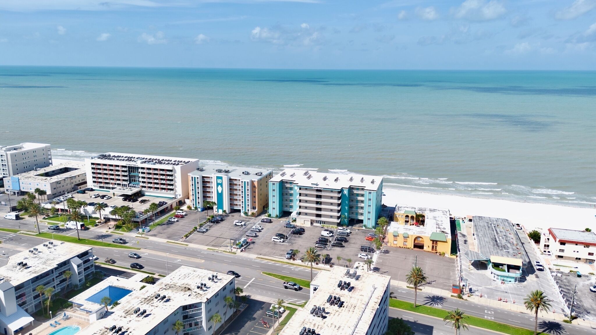Un hotel sulla costa con diversi edifici, un parcheggio e vista sulla spiaggia.