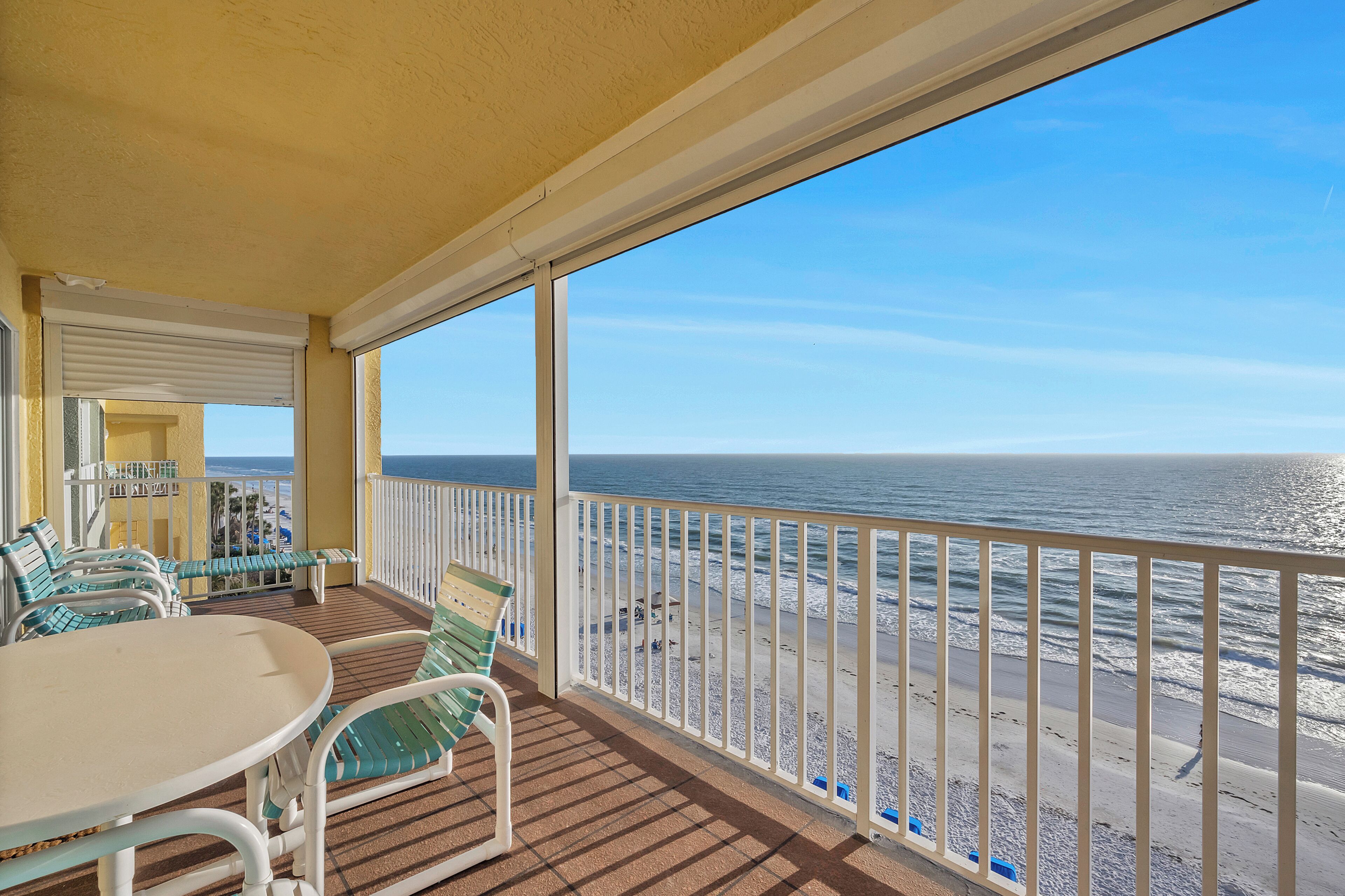 A balcony with a table and chairs, overlooking a beach with a railing.