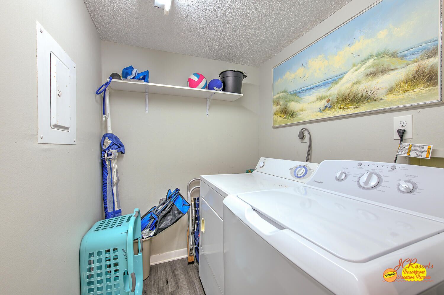 A laundry room with a washing machine, a shelf with sports balls, and a beach painting.
