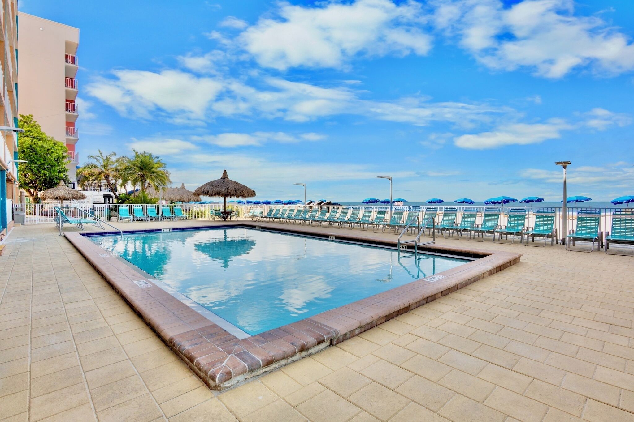 A swimming pool with lounge chairs, a thatched umbrella, and a view of the ocean.