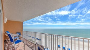 Balcón con sillas azules y una mesa, con vista a una playa y una barandilla.