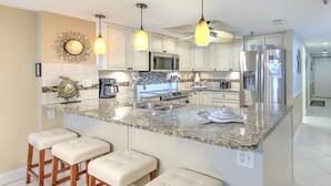 Una cocina moderna con una isla central, taburetes de bar, electrodomésticos de acero inoxidable e iluminación colgante.