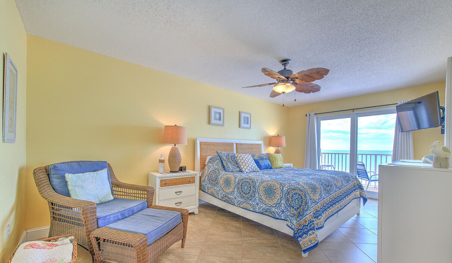 A bedroom with a bed, two nightstands, a chair, a ceiling fan, and a TV.