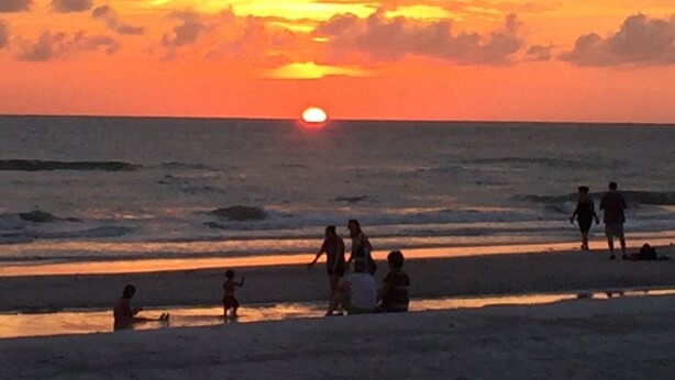 Un atardecer sobre el océano con gente en la playa.