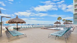 A poolside area with lounge chairs, umbrellas, and a view of the ocean.