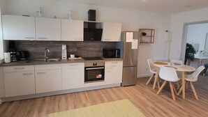 A modern kitchen with white cabinets, a stainless steel refrigerator, a microwave, and a dining area with a round table and chairs. - Apartment 'Rike' with Shared Terrace, Shared Garden and Wi-Fi (Oesterdeichstrich)