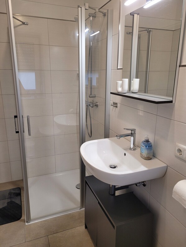 Un baño moderno con ducha de vidrio, un lavamanos blanco y un espejo encima.