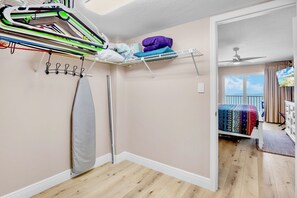 A bedroom with a bed, a ceiling fan, a shelf with folded clothes, and a view of the outdoors.