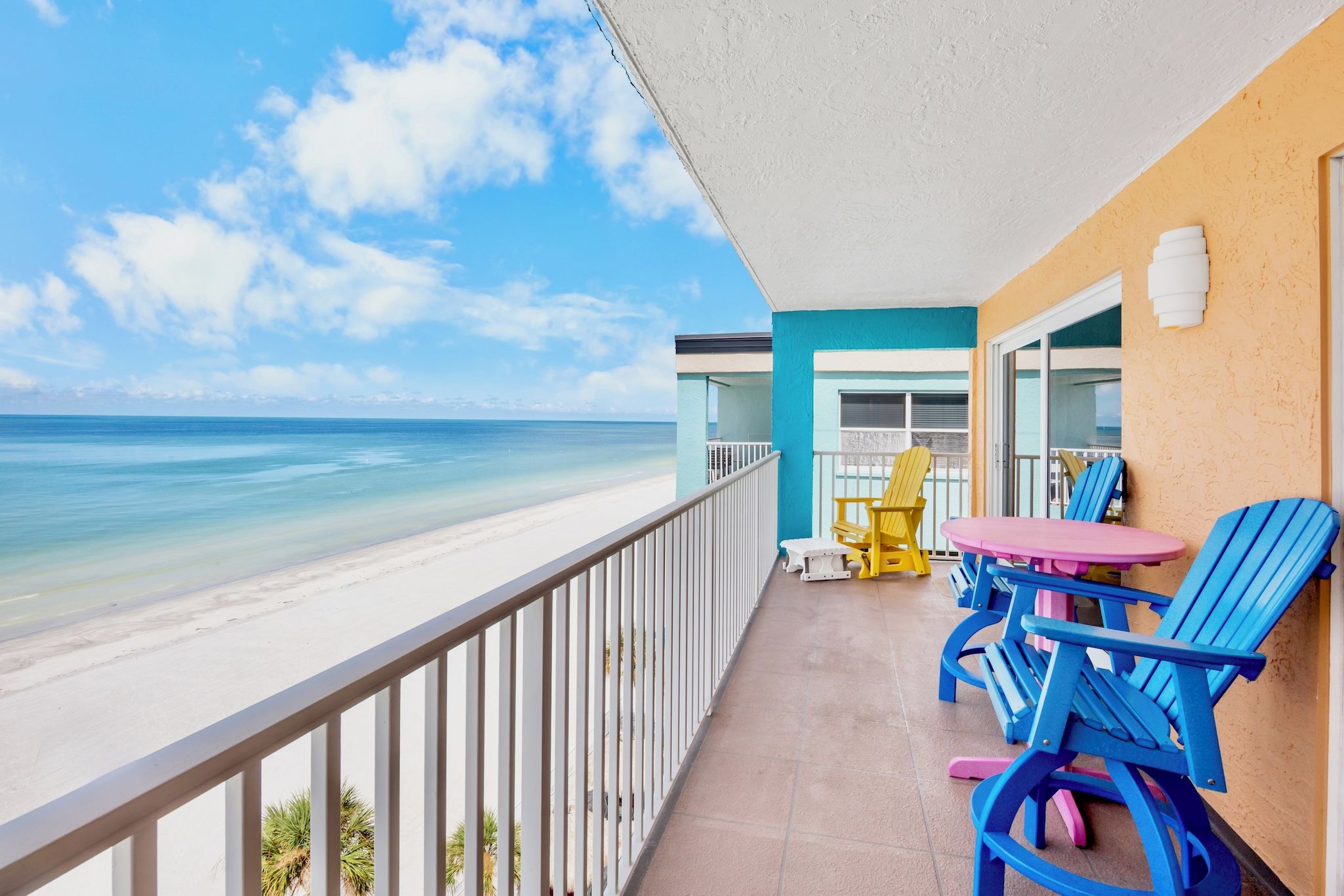 A balcony with a view of the beach, a table with chairs, and a yellow chair.