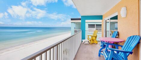 A balcony with a view of the beach, a table with chairs, and a yellow chair.