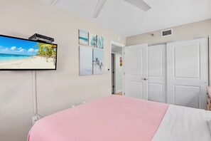 Une chambre à coucher avec un lit, un téléviseur fixé au mur et une porte donnant sur une autre pièce.