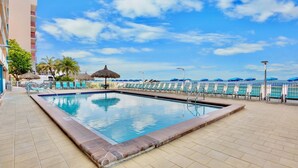 A swimming pool with lounge chairs, a thatched umbrella, and a view of the ocean. - Top Floor Gulf Front Condo w/ Big Balcony - RS614 (N. Redington Beach)