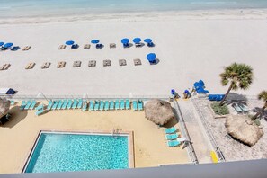 Ein Poolbereich mit Liegestühlen und Sonnenschirmen, ein Sandstrand und ein freier Blick auf den Ozean.