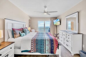 A hotel room with a bed, a dresser, a television, and a balcony with a view of the sea.