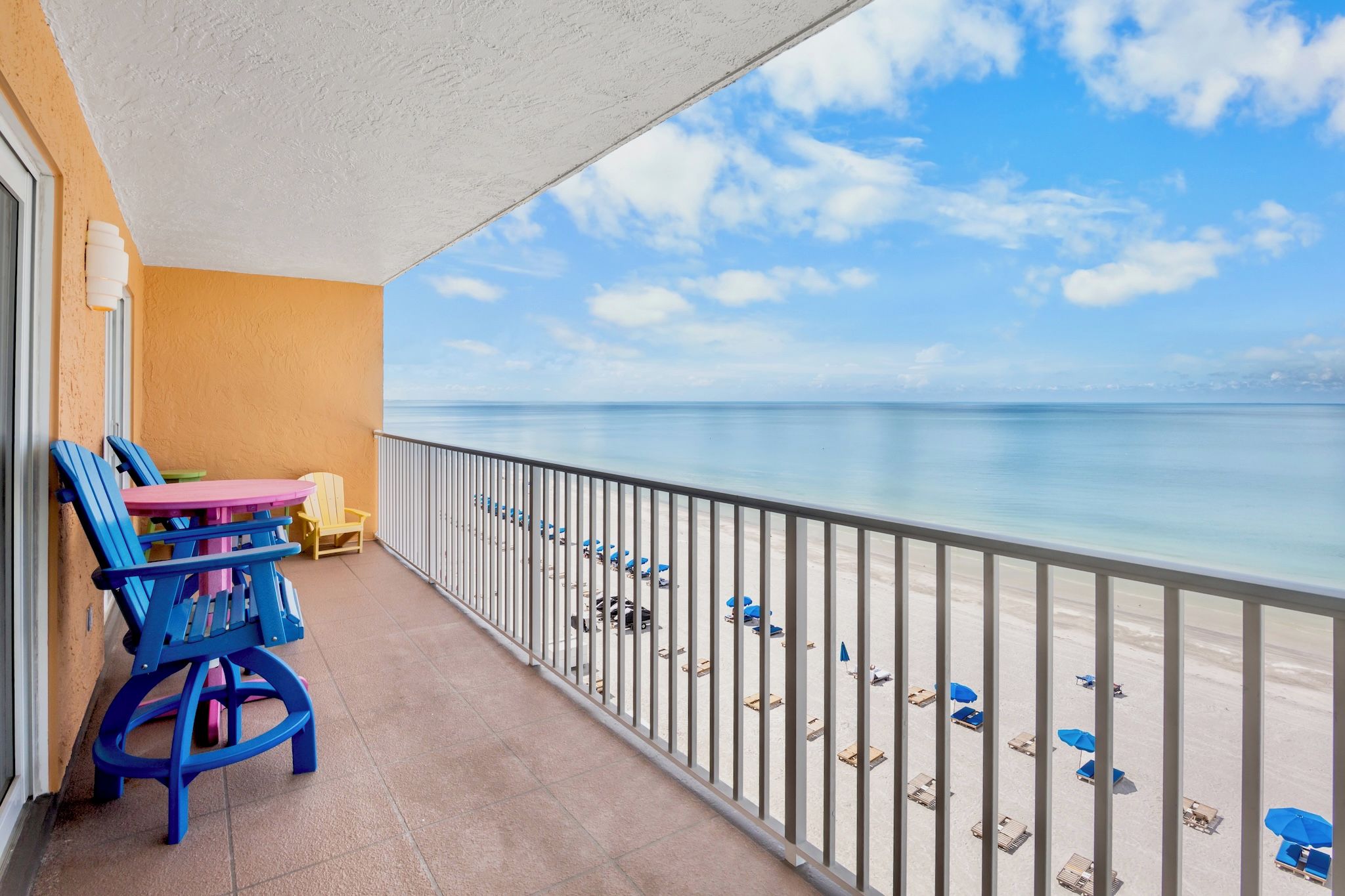 A balcony with a view of the beach, a table with chairs, and a railing.