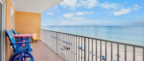 Un balcón con vista a la playa, una mesa con sillas y una barandilla.