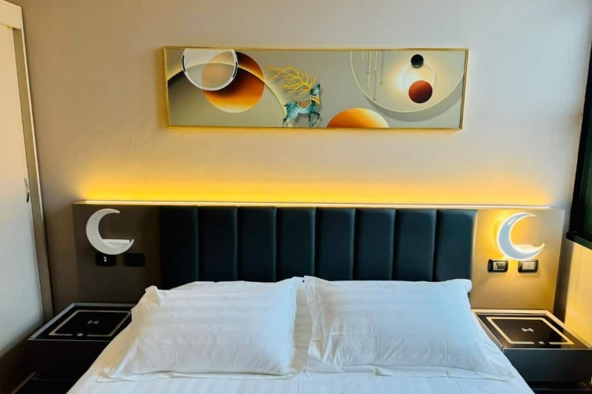 A hotel room with a bed, a headboard with a crescent moon design, and a wall-mounted artwork featuring abstract shapes and a horse.