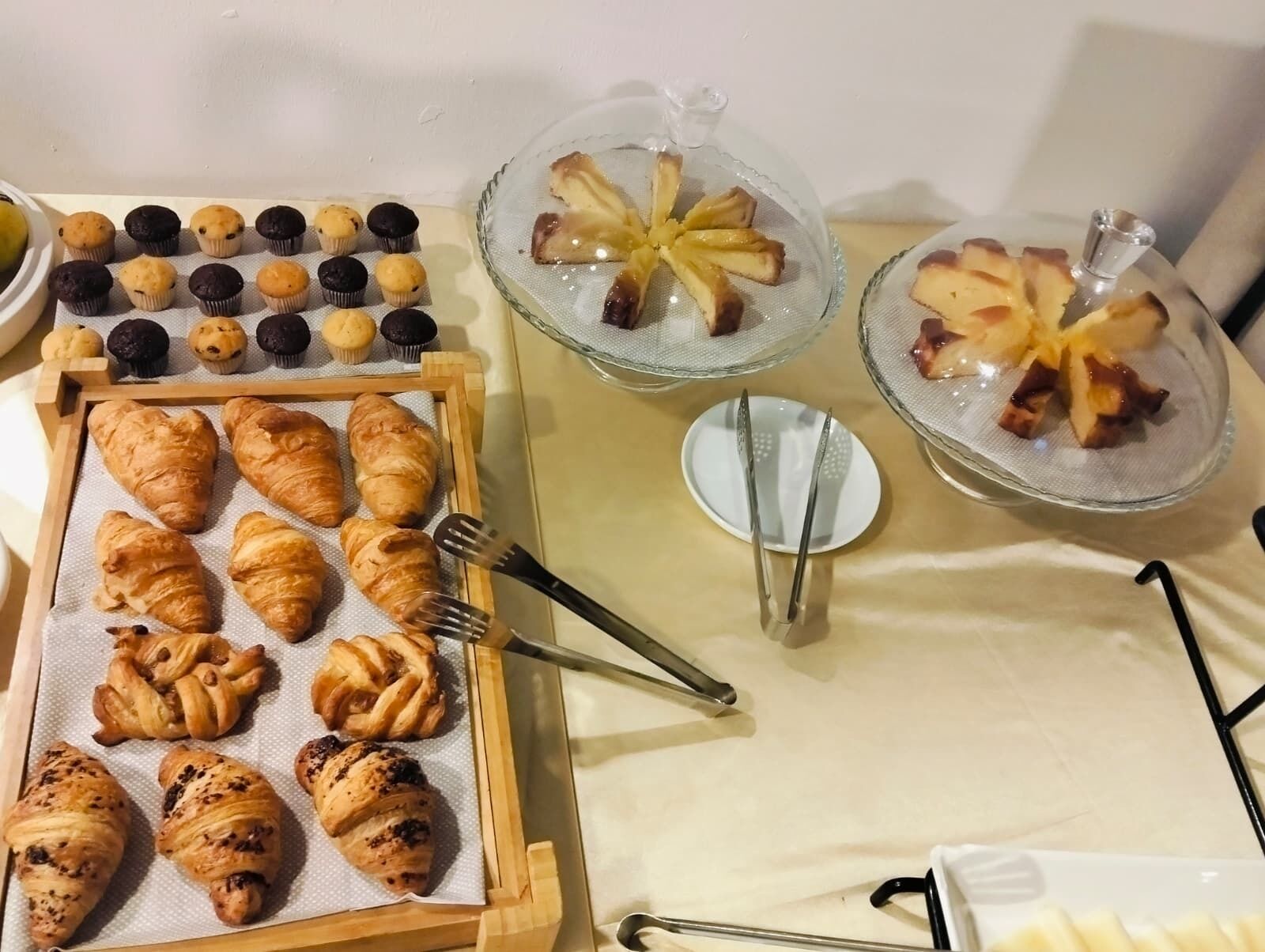 Une variété de viennoiseries, notamment des croissants, des muffins et des pâtisseries, présentées sur des plateaux et dans des récipients en verre.