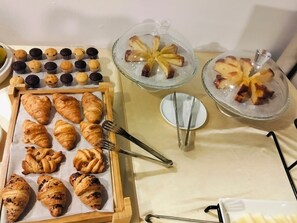 A variety of baked goods including croissants, muffins, and pastries displayed on trays and in glass containers.