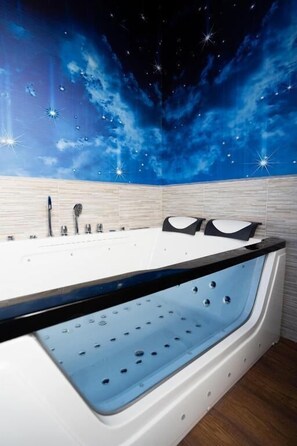 A modern bathroom with a starry sky mural, a large bathtub, and a wooden floor.