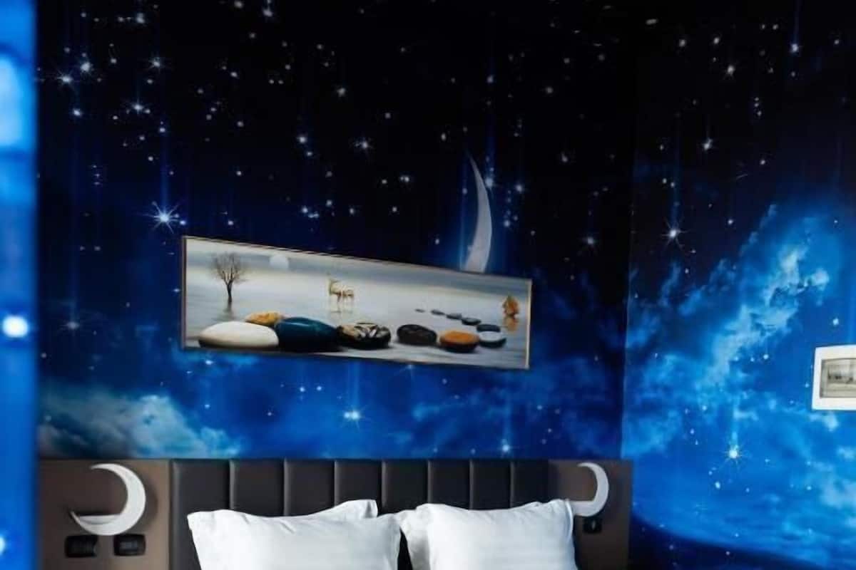 A bedroom with a bed, night sky mural, and a framed picture on the wall.