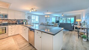 A spacious kitchen with white cabinetry, a large island, and a dining area with a gray sofa and table.
