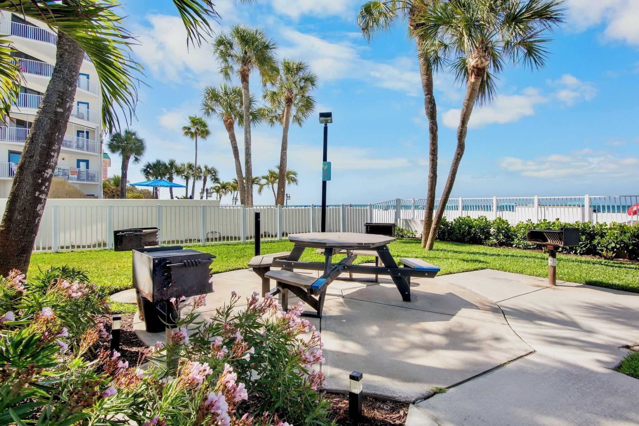 A picnic table with benches, surrounded by palm trees and a white fence.