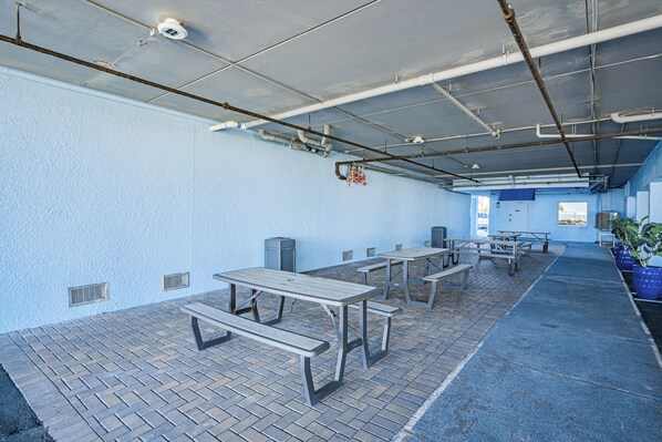 A covered outdoor area with picnic tables and benches, a blue wall, and a ceiling with exposed pipes.