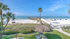 A beach view with a wooden boardwalk, palm trees, and beach chairs.