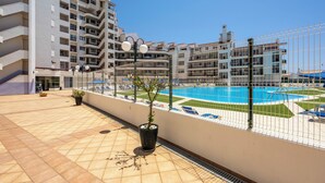 A rooftop pool area with a clear blue sky, a pool, and a building with multiple balconies.