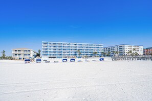 A beachfront hotel with multiple floors, a sandy beach in front, and a clear blue sky.